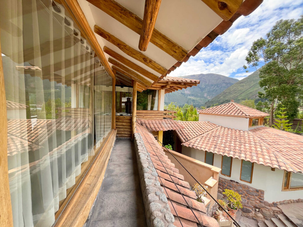 View from a rustic balcony with wooden beams and railings, overlooking terracotta-tiled rooftops and the lush, mountainous landscape beyond