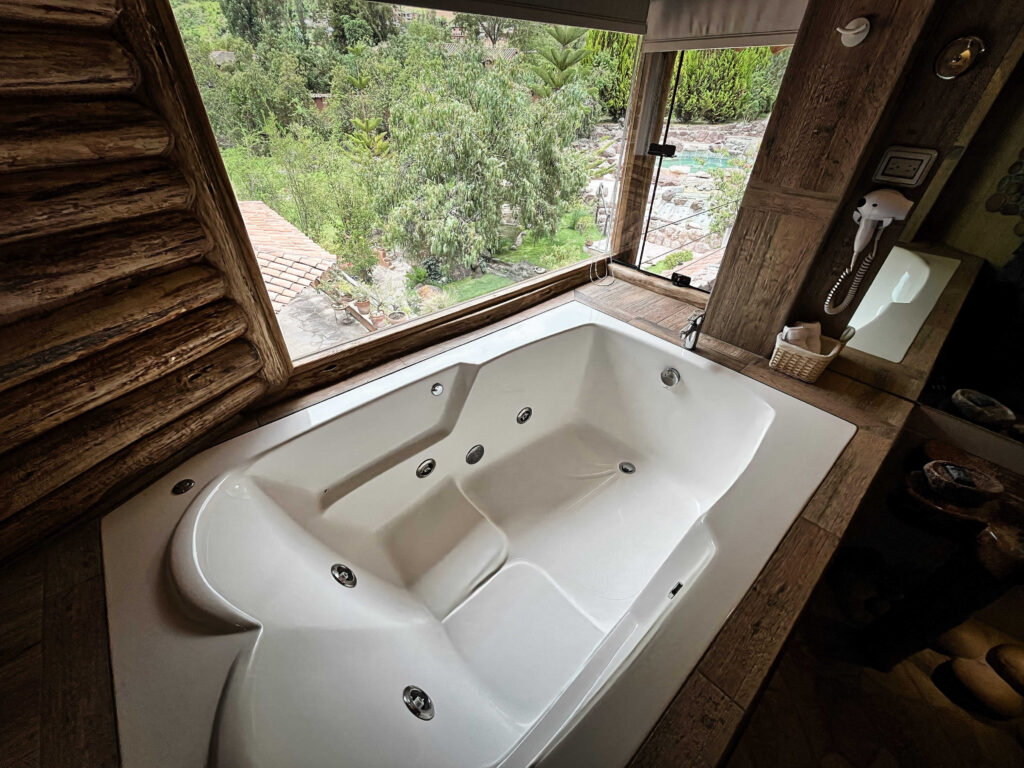 Inviting corner jacuzzi with a view of lush gardens, framed by rustic wooden elements, blending luxury with the natural serenity of the retreat.