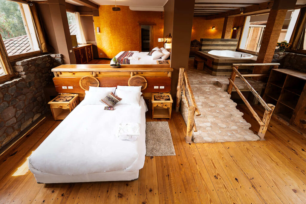 A spacious suite blends rustic charm with luxury, featuring a log bed and a raised Jacuzzi bath area, in an ayahuasca retreat