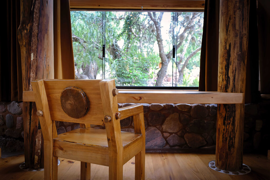 A rustic wooden chair by a window overlooks a tranquil forest, blending craftsmanship with the natural beauty outside