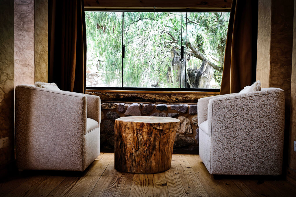 Two elegant armchairs flank a natural wood table, creating a cozy nook with a picturesque window view of lush greenery