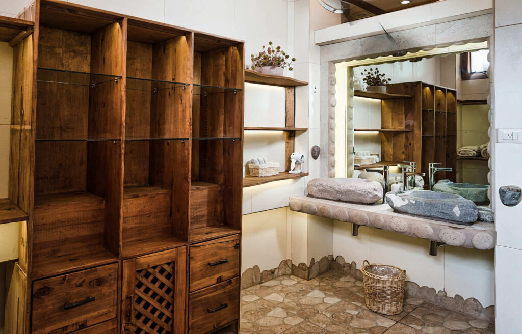 A rustic bathroom pairs wood shelving with a stone countertop basin, mirrored by an ornate frame, enhancing the natural, earthy ambiance