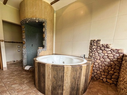 A rustic yet elegant bathroom with a corner jacuzzi tub encased in wood, next to a stone- lined shower area, exuding a serene, spa-inspired ambiance with a touch of natural luxury