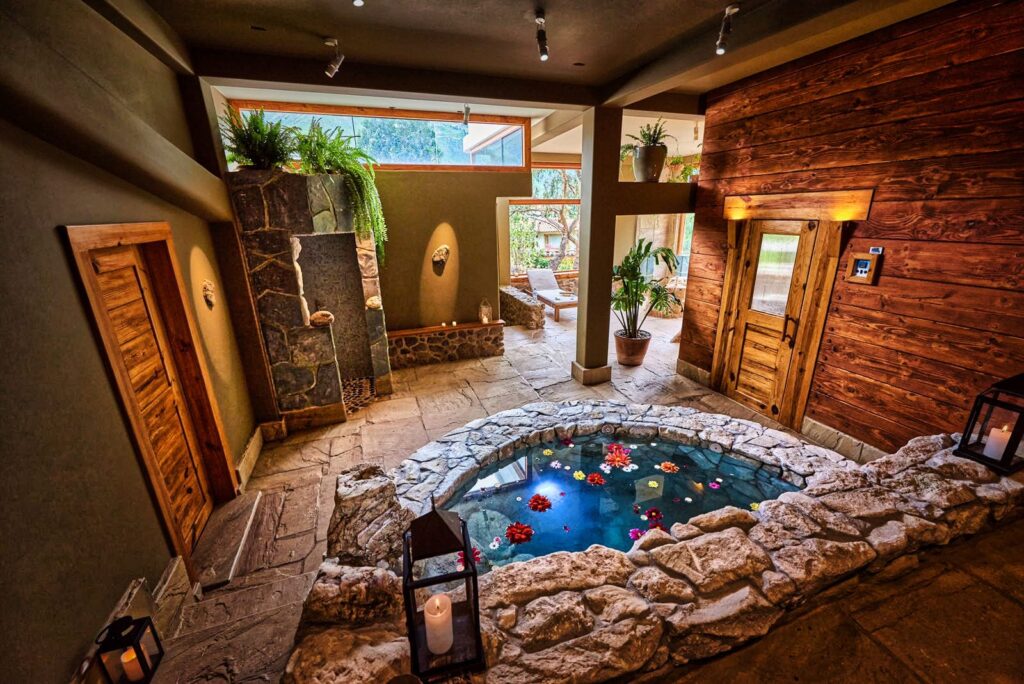 a cozy indoor spa area with a central stone-rimmed pool adorned with floating flowers, complemented by warm wooden accents and natural light.