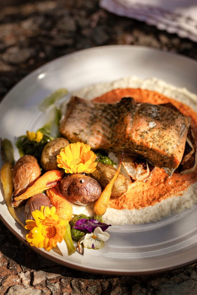 an elegantly plated meal consisting of a perfectly cooked piece of salmon with crisp skin, accompanied by roasted baby potatoes and carrots, all artfully arranged on a creamy base.